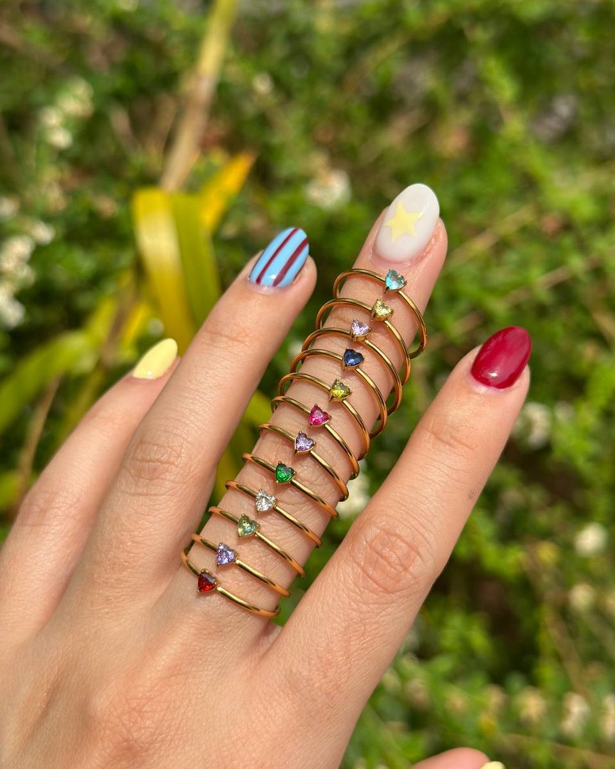 Los doce Heart Birthstone Ring dorados puestos en un dedo, uno por mes
